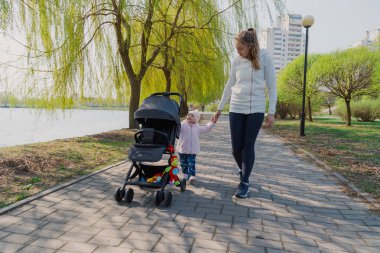 Genç bir anne bebek arabası yuvarlayan bir çocukla yürüyor..