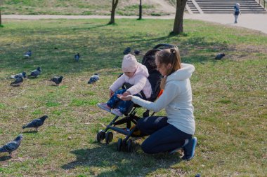 Bebek arabasında bebekli genç bir anne güvercinleri besliyor..