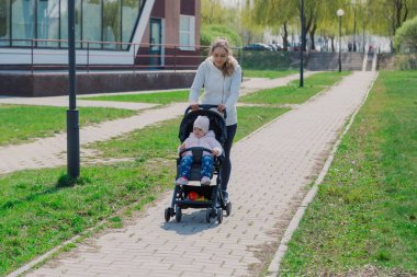 Young mother with a baby in a stroller in a summer park.