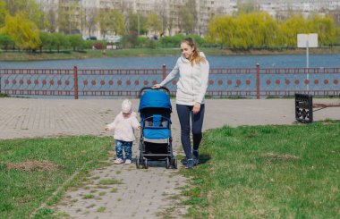 Genç bir anne bebek arabası yuvarlayan bir çocukla yürüyor..
