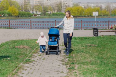 Genç bir anne bebek arabası yuvarlayan bir çocukla yürüyor..