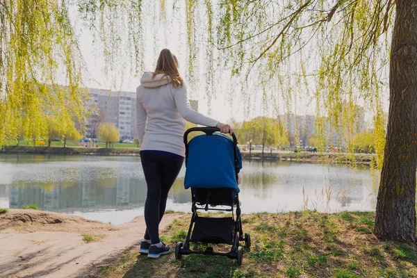 Joven madre con un bebé en un cochecito junto al lago en verano . — Foto de Stock