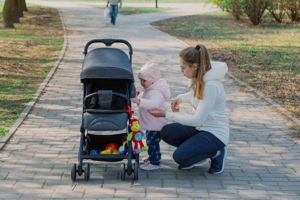 Una madre joven camina con un niño que rueda un cochecito . — Foto de Stock