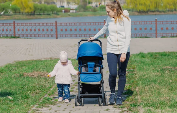 Молодая мать гуляет с ребенком, который катает коляску . — стоковое фото
