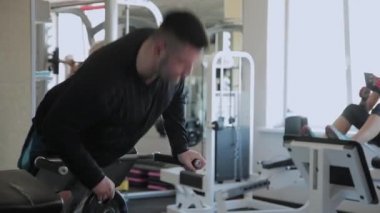 Kilolu yetişkin bir adam bir spor salonunda hiperuzantısı gerçekleştirir.