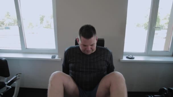 Adult man with overweight presses his legs on the simulator. — Stock Video