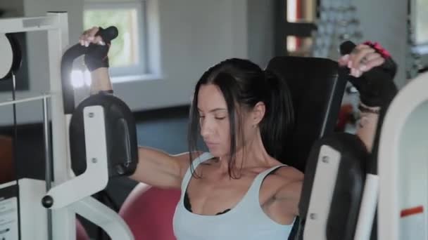 Belle femme sportive entraîne les muscles pectoraux sur le simulateur . — Video