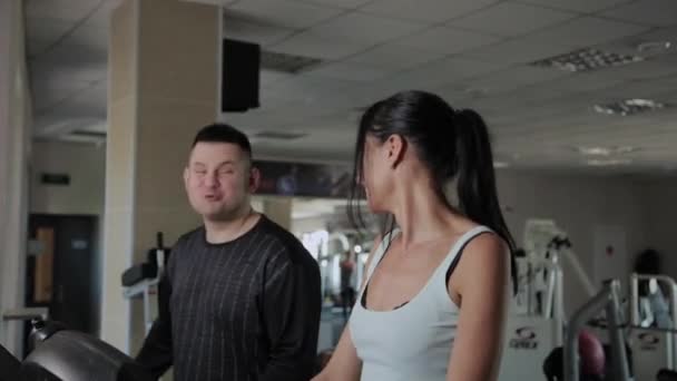 Mooie atletische vrouw en een man met overgewicht zijn training op een loopband. — Stockvideo