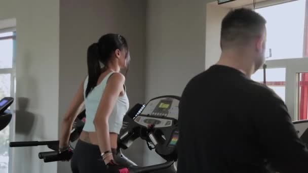 Vacker atletisk kvinna och en man med övervikt är träning på ett löpband. — Stockvideo