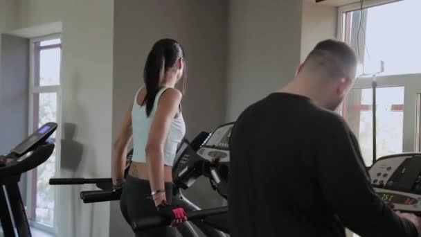 Vacker atletisk kvinna och en man med övervikt är träning på ett löpband. — Stockvideo