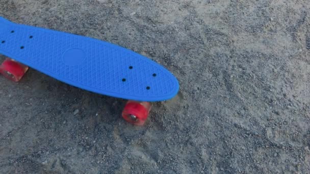 Скейтборд стоит на песке в ясную погоду . — стоковое видео