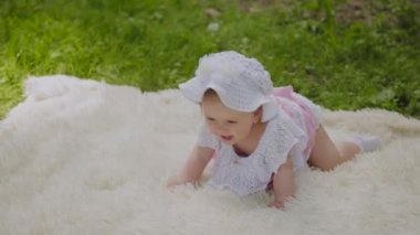 Parkta yatak örtüsü üzerinde oynayan çok küçük ve güzel bir kız.