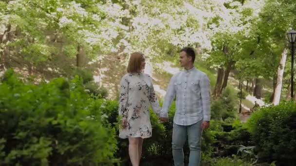 Beautiful happy young couple walking through the park in sunny weather. — Stock Video