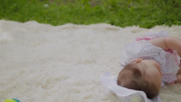 Una ragazza molto piccola e bella che gioca sul copriletto nel parco . — Video Stock