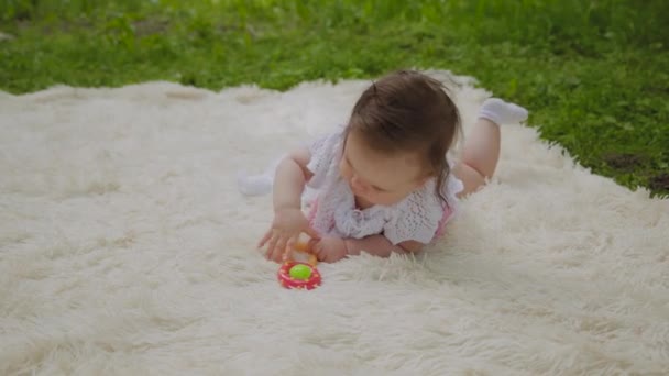 Una ragazza molto piccola e bella che gioca sul copriletto nel parco . — Video Stock