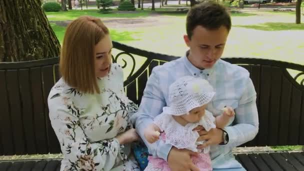 Un niño feliz come palitos de maíz en un banco en el parque con sus padres . — Vídeo de stock