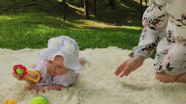 Una ragazza molto piccola e bella che gioca sul copriletto nel parco . — Video Stock