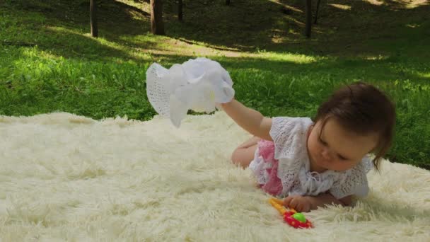 Uma menina muito pequena e bonita brincando na colcha no parque . — Vídeo de Stock