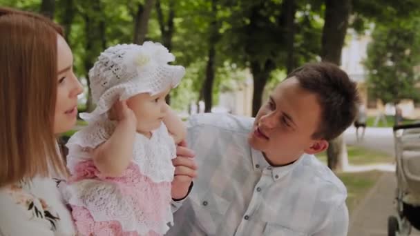 Feliz familia joven con su hijo descansando en el parque en el verano en un banco. Una hermosa mujer con su marido y un niño sentado en un banco en el fondo del paisaje urbano — Vídeo de stock