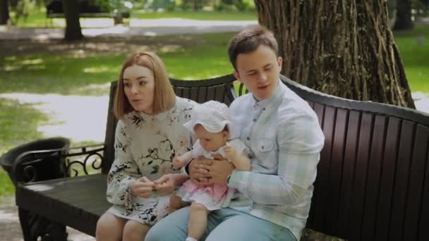 Un niño feliz come palitos de maíz en un banco en el parque con sus padres . — Vídeo de stock