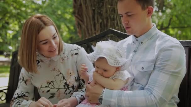 Un niño feliz come palitos de maíz en un banco en el parque con sus padres . — Vídeos de Stock