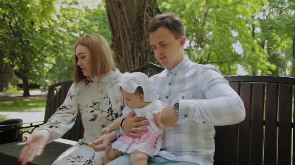 Küçük mutlu bir çocuk ailesiyle parkta bir bankta mısır çubukları yiyor.. — Stok video