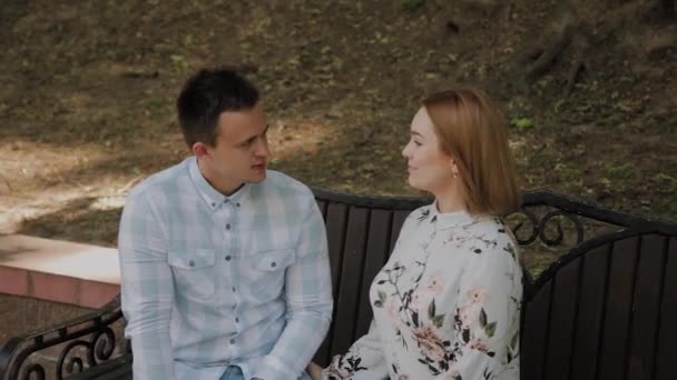 Aşık güzel mutlu çift parkta bir bankta oturan ve konuşurken. — Stok video