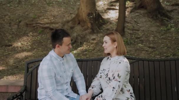 Aşık güzel mutlu çift parkta bir bankta oturan ve konuşurken. — Stok video