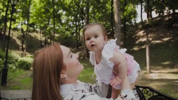 Bela jovem mãe feliz segurando sua filha em seus braços no parque . — Vídeo de Stock