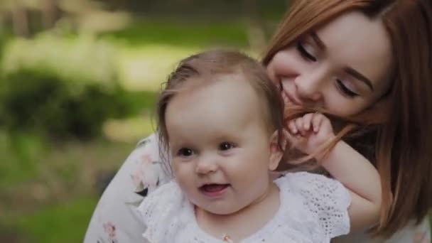 Bela jovem mãe feliz segurando sua filha em seus braços no parque . — Vídeo de Stock