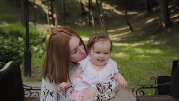 Hermosa madre joven feliz sosteniendo a su hija en sus brazos en el parque . — Vídeo de stock