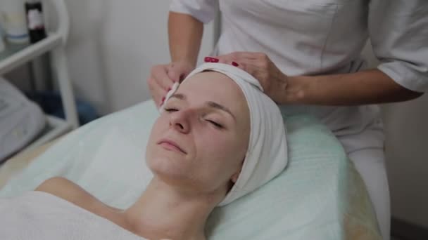 Eine schöne Kosmetikerin reibt ihr Gesicht vor dem Eingriff mit einem Wattepad ein. — Stockvideo