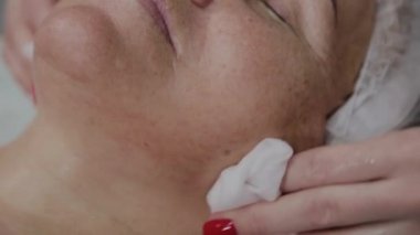 Güzellik uzmanı, bir kozmetoloji kliniğinde yaşlı bir kadının yüzünü yıkama işlemini gerçekleştirir.