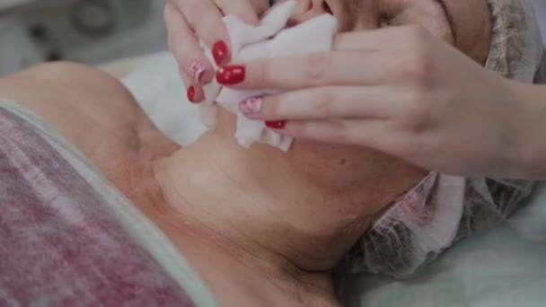 Kozmetikus végrehajtja az eljárást a mosás az arc egy idős nő a kozmetológiai klinikán. — Stock videók