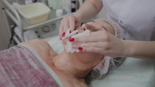 Αισθητικός εκτελεί τη διαδικασία του πλυσίματος του προσώπου μιας γηραίας γυναίκας σε μια κλινική κοσμετολογίας. — Αρχείο Βίντεο