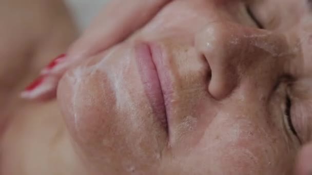 Cosmetóloga femenina haciendo masaje facial a anciana en clínica cosmetológica . — Vídeo de stock