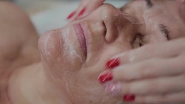 Cosmetóloga femenina haciendo masaje facial a anciana en clínica cosmetológica . — Vídeo de stock