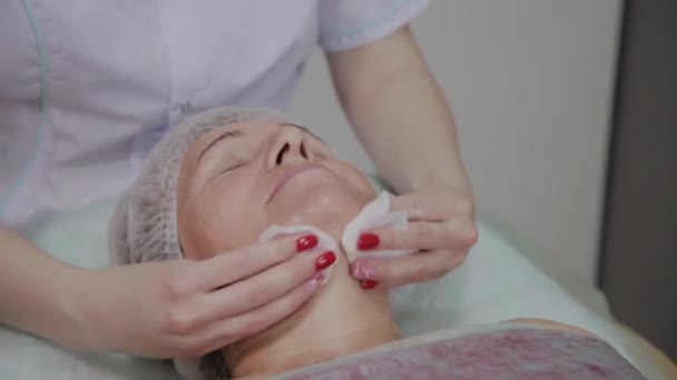 Kosmetikerin führt in einer kosmetologischen Klinik das Waschen des Gesichts einer älteren Frau durch. — Stockvideo