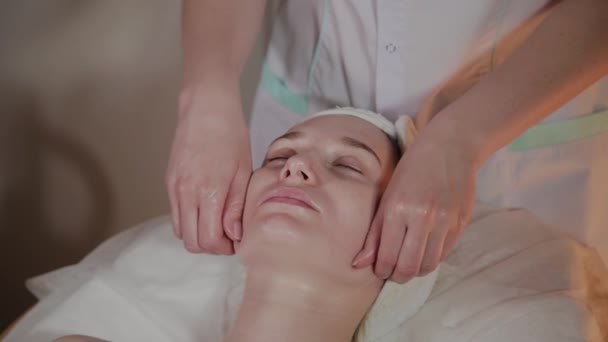 Esteticista profissional faz uma massagem complexa para uma jovem no escritório de cosmetologia . — Vídeo de Stock