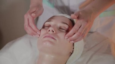 Profesyonel güzellik kozmetoloji ofisinde genç bir kız için karmaşık bir masaj yapar.