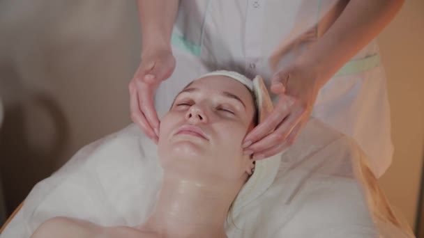Esteticista profesional hace un masaje complejo a una joven en la oficina de cosmetología . — Vídeo de stock