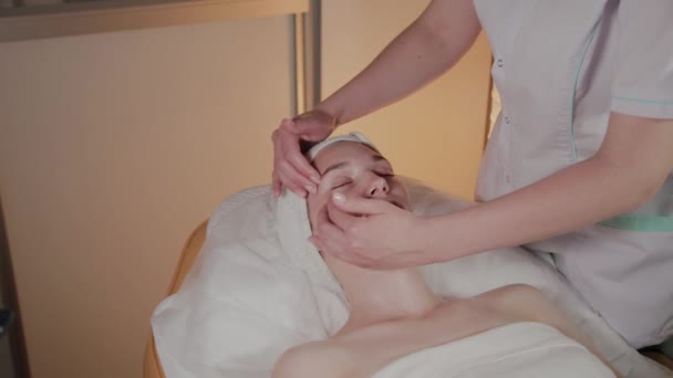 Esteticista profissional faz uma massagem complexa para uma jovem no escritório de cosmetologia . — Vídeo de Stock