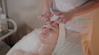 Profesyonel güzellik kozmetoloji ofisinde genç bir kız için karmaşık bir masaj yapar.