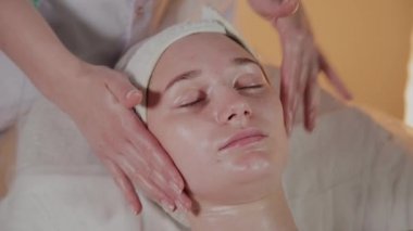 Profesyonel güzellik kozmetoloji ofisinde genç bir kız için karmaşık bir masaj yapar.