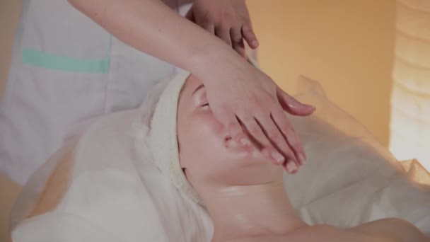 Esteticista profissional faz uma massagem complexa para uma jovem no escritório de cosmetologia . — Vídeo de Stock