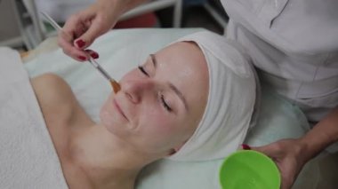 Profesyonel kozmetolojist hastaların yüzüne maske takıyor.