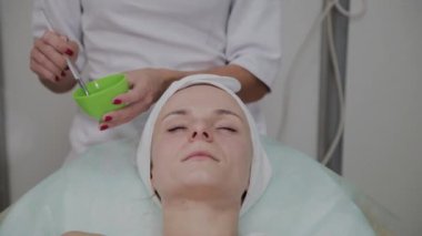 Profesyonel kozmetolojist hastaların yüzüne maske takıyor.