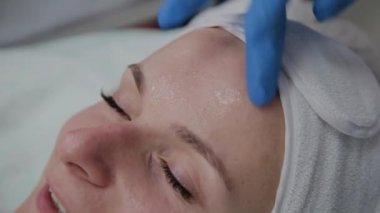 Profesyonel kozmetolojist hastaların yüzüne serum uygular.