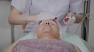 Güzellik uzmanı, bir kozmetoloji kliniğinde yaşlı bir kadının yüzünü yıkama işlemini gerçekleştirir.