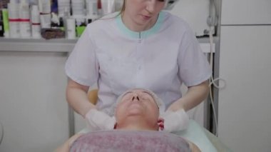 Güzellik uzmanı, bir kozmetoloji kliniğinde yaşlı bir kadının yüzünü yıkama işlemini gerçekleştirir.